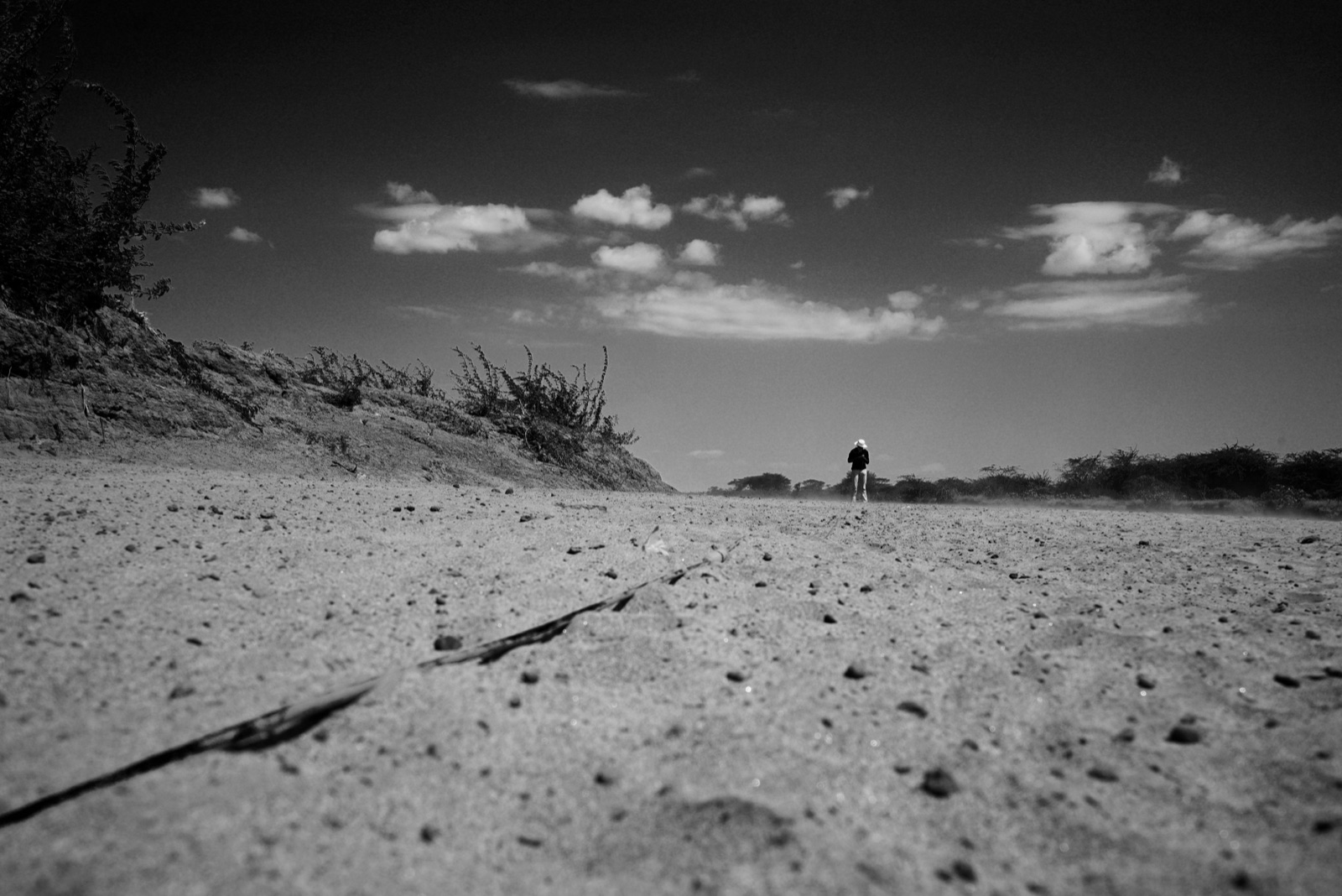 A figure walking a dry, sandy riverbed