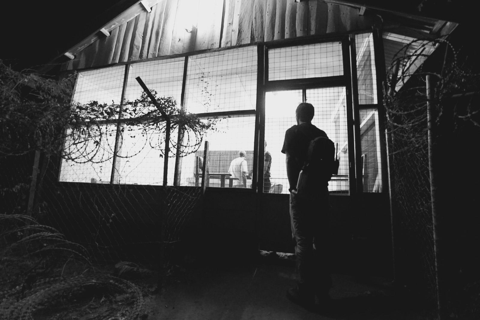A person standing at the lit doorway of a screened building at night