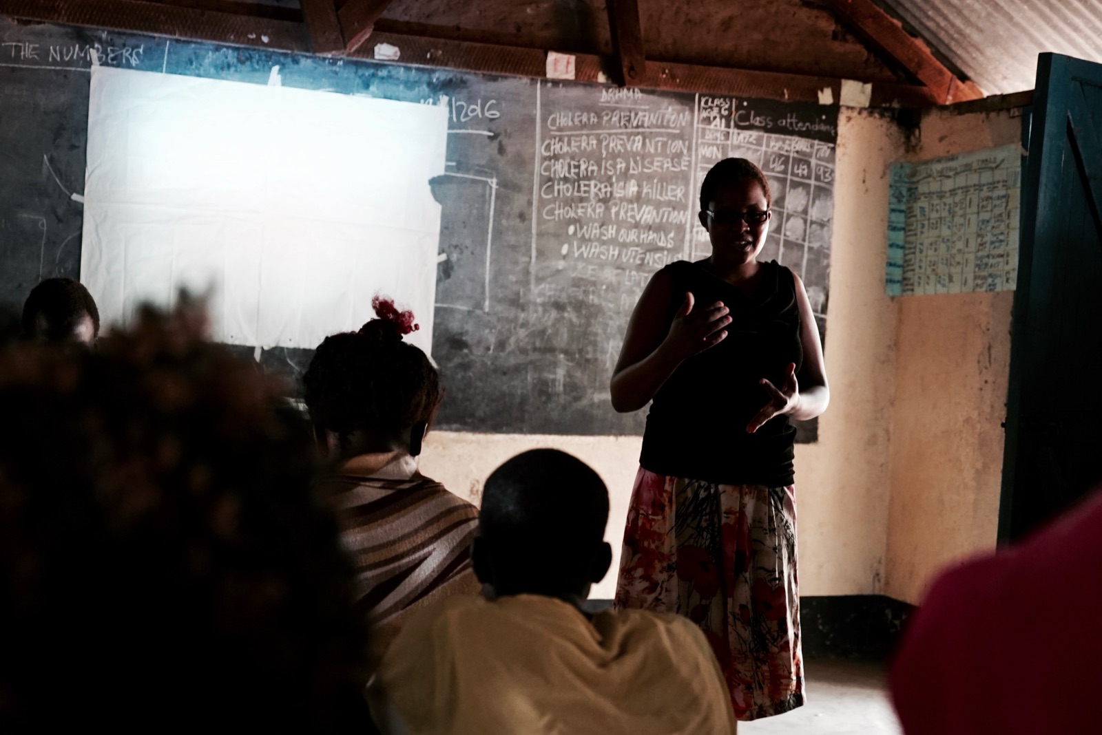 A woman teaching a cholera-prevention class at a chalkboard