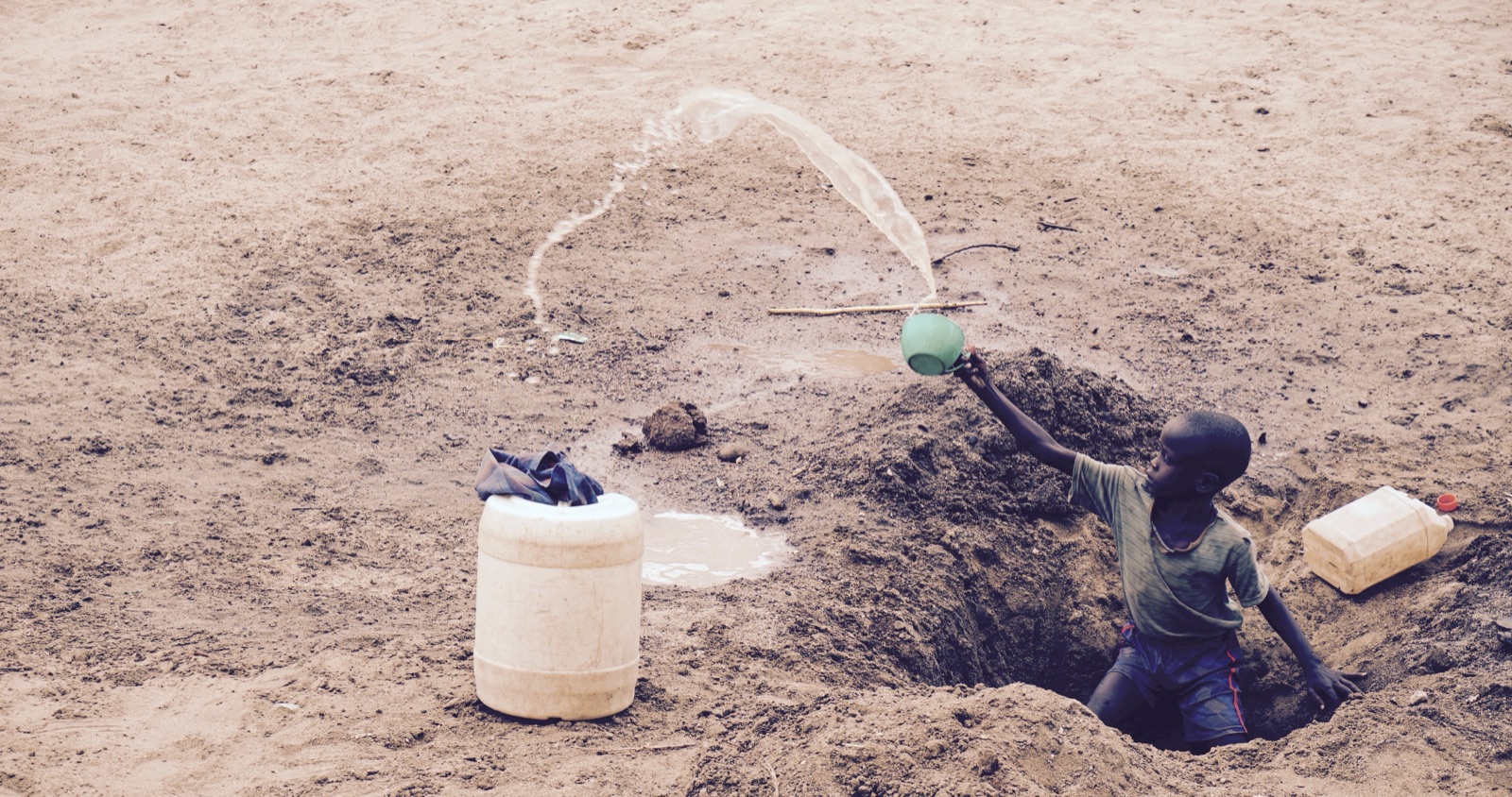 A boy in a shallow well pours water into a plastic drum