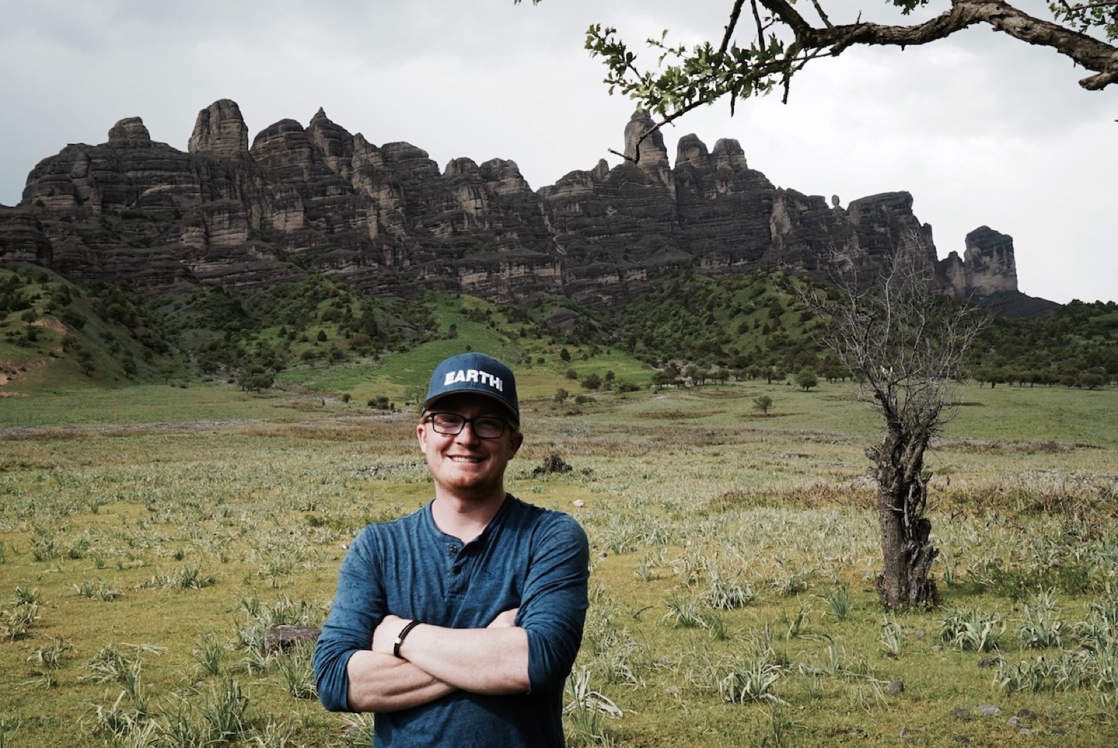 Brendan in the field, green hills and rock towers behind him