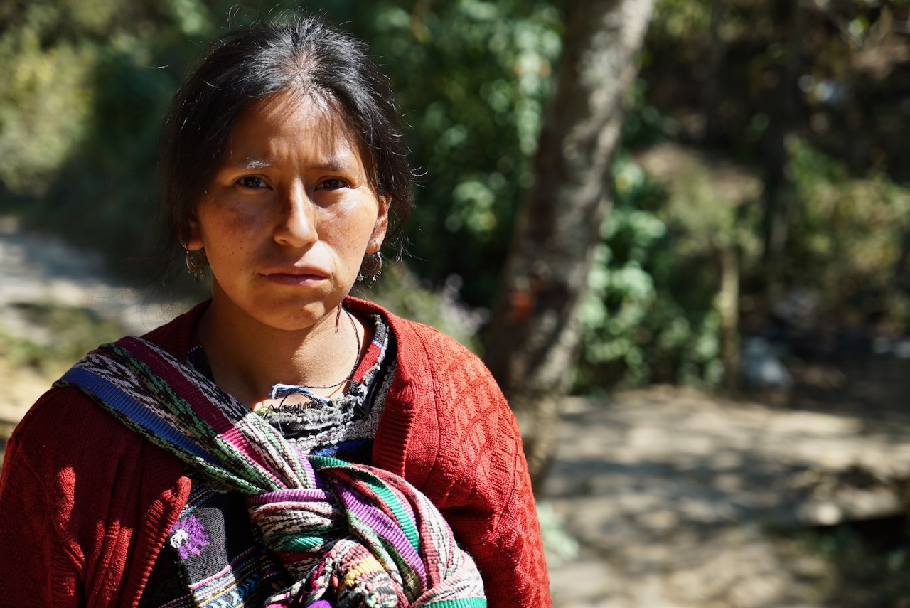 A woman in a red cardigan and woven wrap, standing on a woodland path