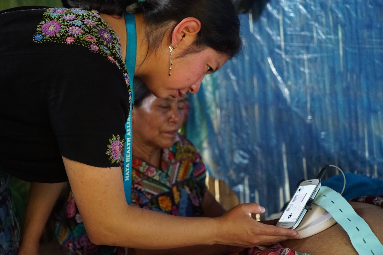 A health worker using a phone and cuff during a home visit