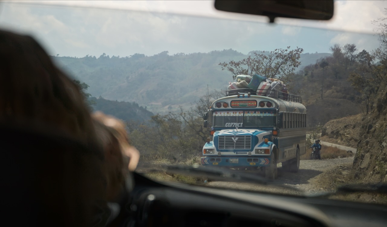 A loaded chicken bus on a mountain road, seen through a windscreen