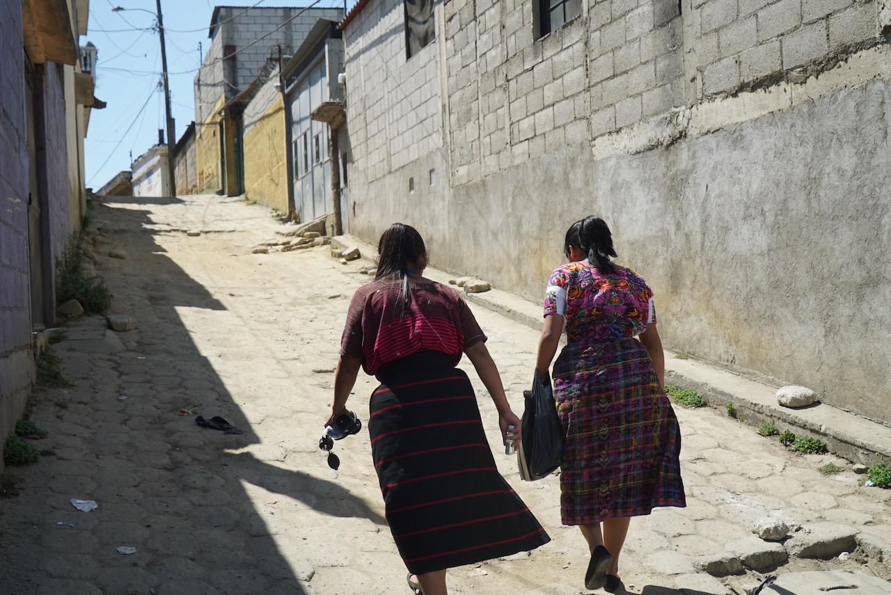 Two women walking up a cobbled street between concrete houses