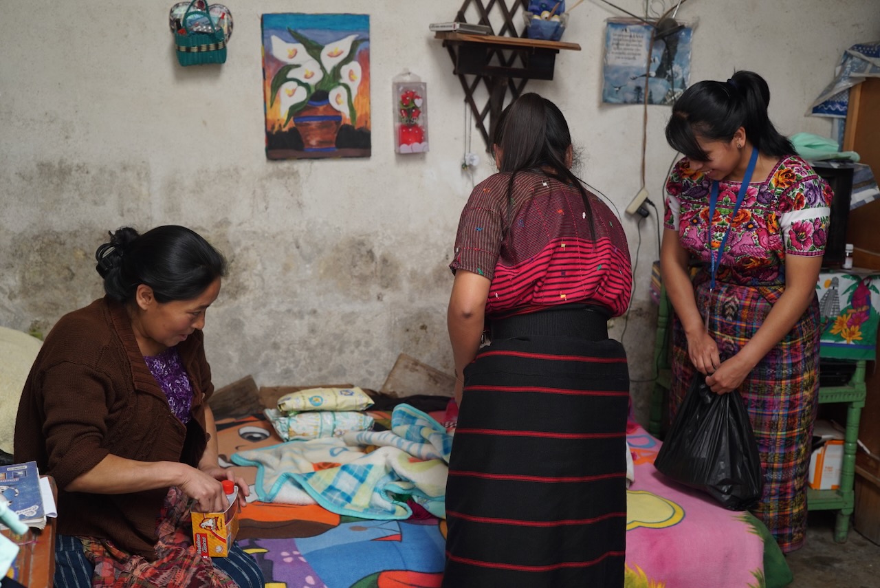 A home visit: three women in a small room with folded blankets on the bed